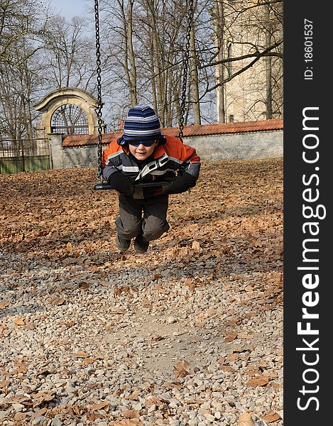 Young child with sunglasses swinging on a chain swing in a playground. Young child with sunglasses swinging on a chain swing in a playground