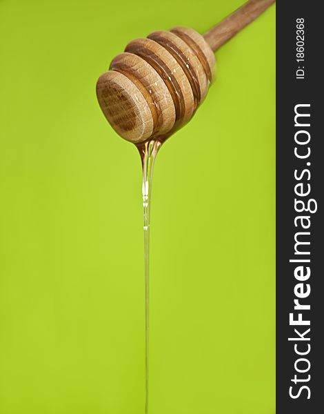 Honey dripping from wooden honey spoon on green background. Honey dripping from wooden honey spoon on green background