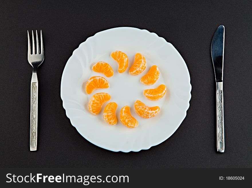 Plate with segments of a tangerine a plug and a knife against a dark background