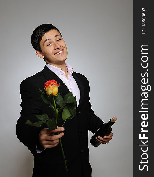 Handsome romantic young man holding rose flower and vine bottle prepared for a valentines day. gray background. Handsome romantic young man holding rose flower and vine bottle prepared for a valentines day. gray background