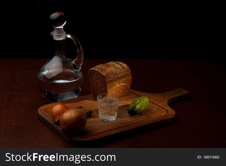 Still life of a decanter of vodka, two onions, cucumber and rye bread