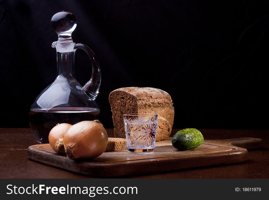 Still life of a decanter of vodka, two onions, cucumber and rye bread