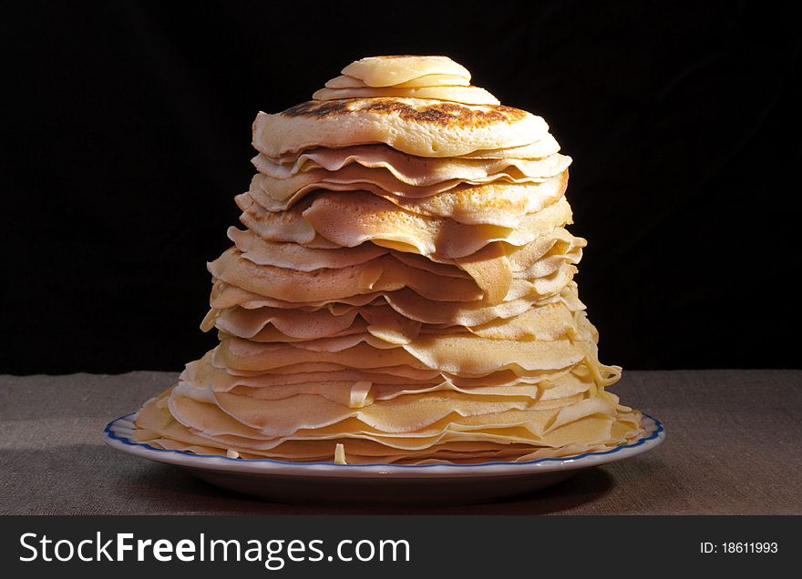 Pile of pancakes with an oil slice on a plate on black