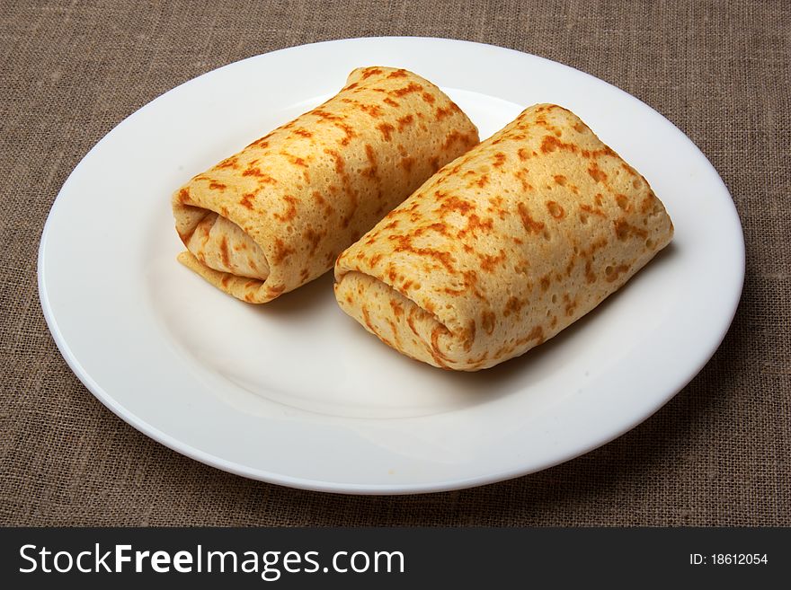 Pancakes with rolled up into a roll, on a white plate on canvas