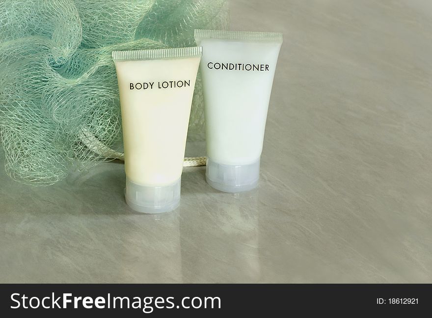 Two tubes of body lotion and body conditioner with a loofah on bathroom tile tabletop. Two tubes of body lotion and body conditioner with a loofah on bathroom tile tabletop.