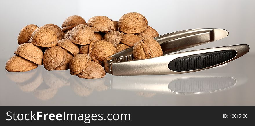 Close-up of walnut's nutshell and nutcracker on neutral background with reflection. Close-up of walnut's nutshell and nutcracker on neutral background with reflection