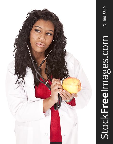 A woman with a stethoscope is listening to an apple and looking to the side. A woman with a stethoscope is listening to an apple and looking to the side.