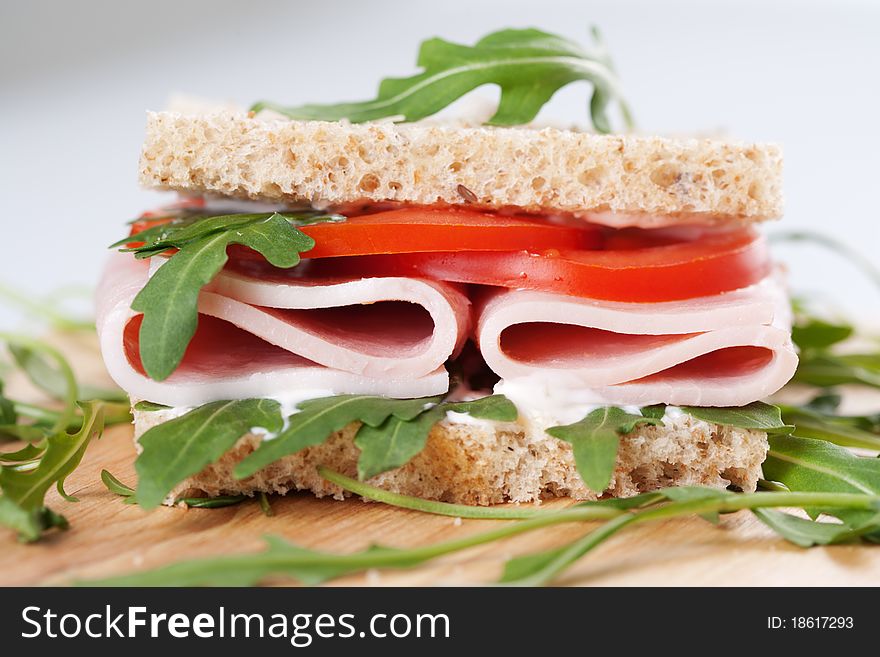 Sandwich with ham,tomato, and rucola salad on the wooden cutting board