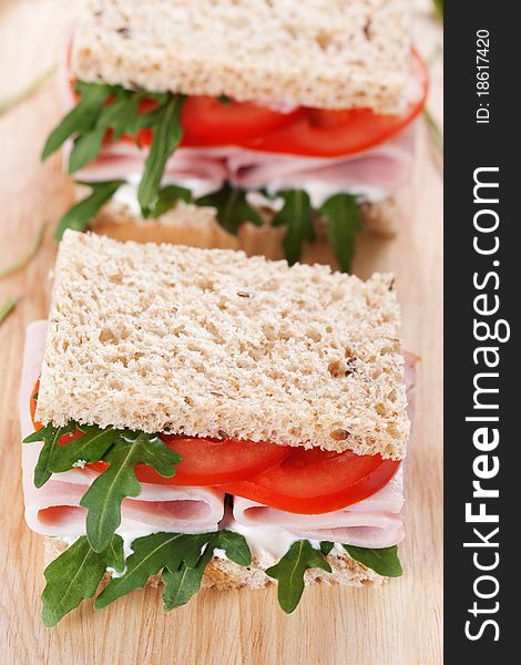 Sandwich with ham,tomato, and rucola salad on the wooden cutting board