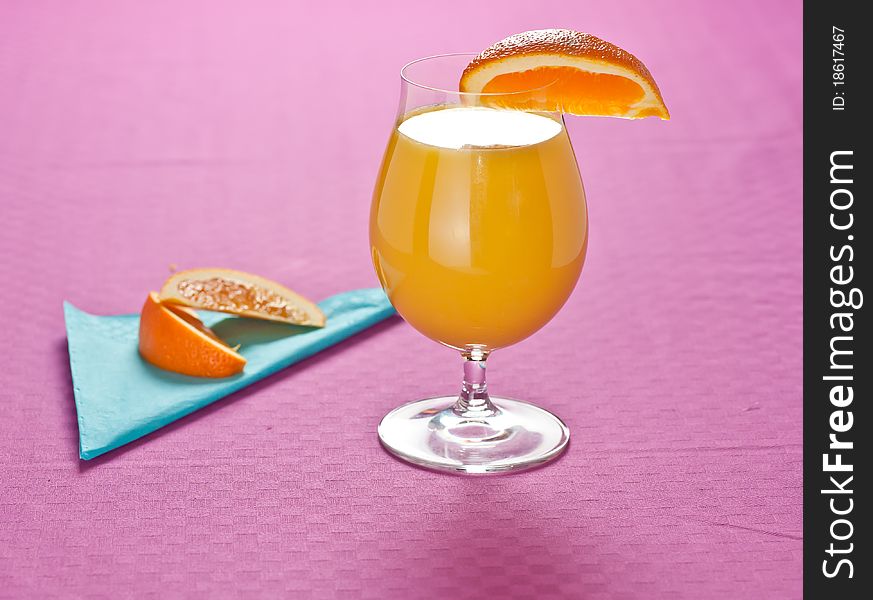 Orange juice with slices of orange on the side, presented on a pastel pink tablecloth