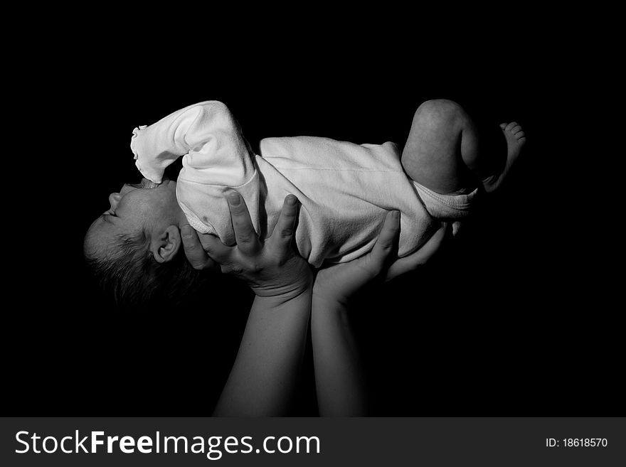 A baby being held in the air. The child is risen above. Image in black and white.