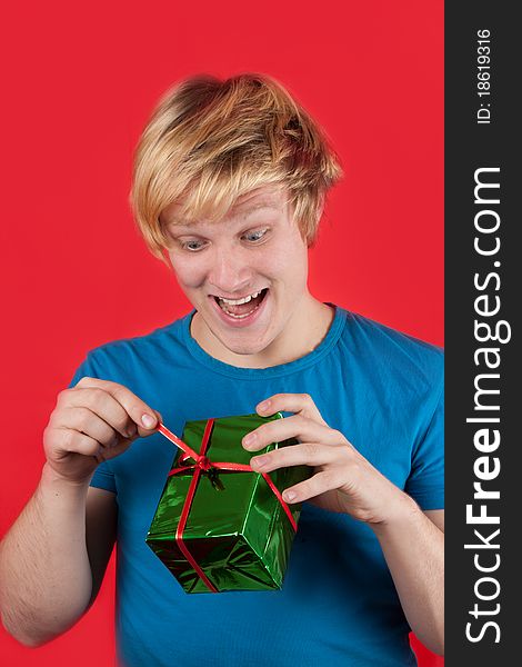 Excited young man opening a present on red background. Excited young man opening a present on red background