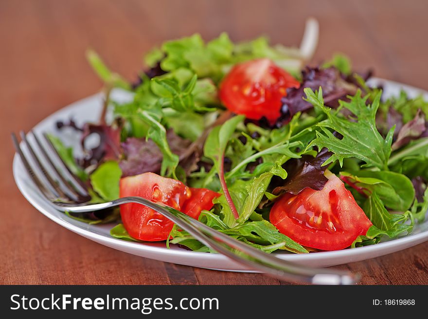 Salad with leafy greens and tomato on rustic, teak table. Salad with leafy greens and tomato on rustic, teak table