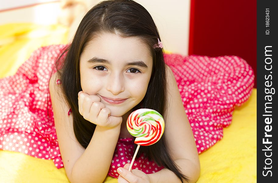Little girl with lollipop in her bedroom.