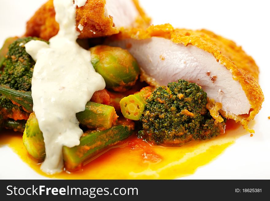 Studio macro close up shoot of tender chicken meat breaded and fried with vegetables in tomato sauce over white. Studio macro close up shoot of tender chicken meat breaded and fried with vegetables in tomato sauce over white