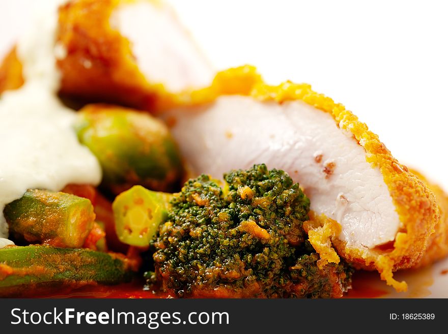 Studio macro close up shoot of tender chicken meat breaded and fried with vegetables in tomato sauce over white. Studio macro close up shoot of tender chicken meat breaded and fried with vegetables in tomato sauce over white