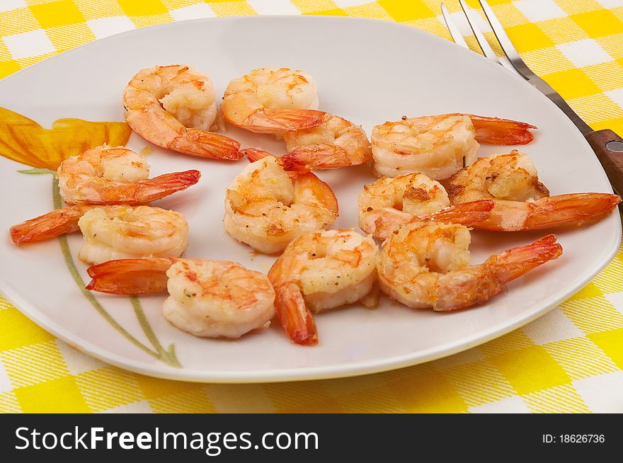 Cooked shrimps on plate with fork and yellow table cloth