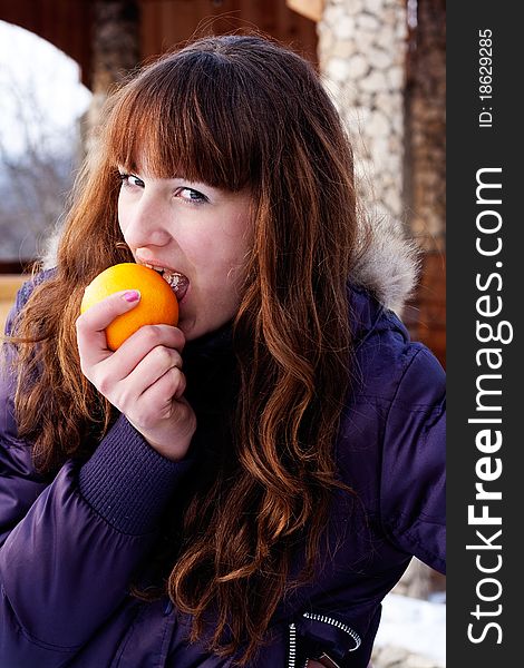 Girl in purple winter jacket eats orange. Girl in purple winter jacket eats orange