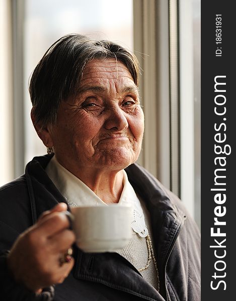 Portrait of Happy Smiling Senior Woman Beside the Window and Drinking Coffee, looking at camera. Portrait of Happy Smiling Senior Woman Beside the Window and Drinking Coffee, looking at camera