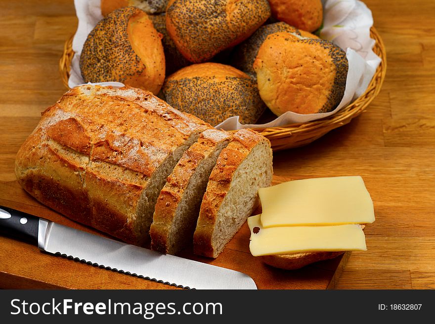 Fresh bread cheese and knife on wooden cutting board with basket with bread rolls in the background. Fresh bread cheese and knife on wooden cutting board with basket with bread rolls in the background