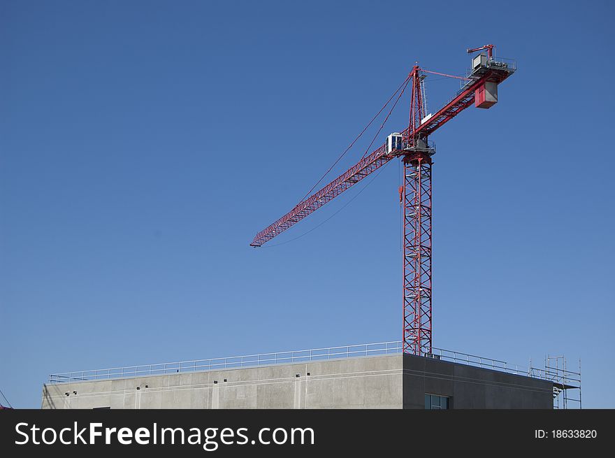 Red construction crane towers above a new concrete structure against a blue sky