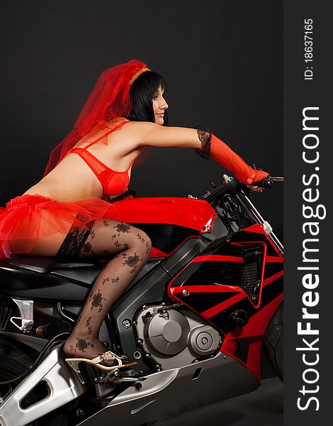 Beautiful dark-haired girl in a red wedding dress on motorbike isolated on black background in studio. Beautiful dark-haired girl in a red wedding dress on motorbike isolated on black background in studio