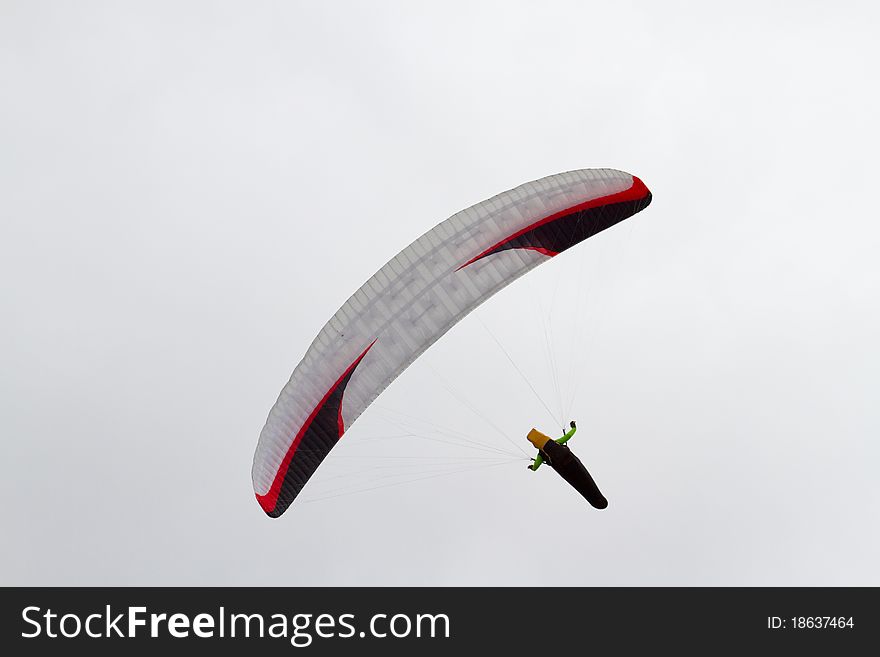 A sole paraglider floating through an overcast sky.