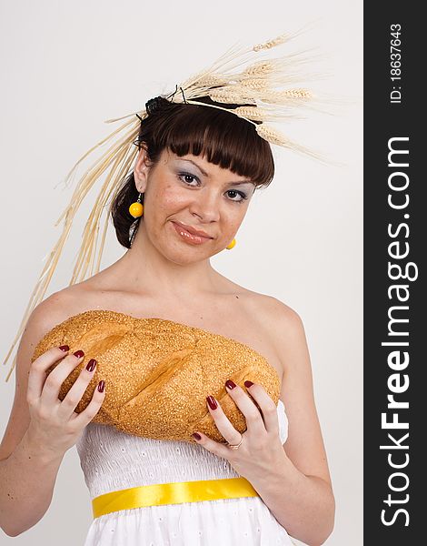 Beautiful brunette girl with ears of wheat in her hair is eating a bread isolated on the white background. Beautiful brunette girl with ears of wheat in her hair is eating a bread isolated on the white background