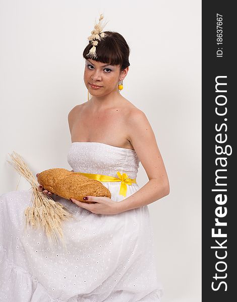 Beautiful brunette girl with ears of wheat in her hair is eating a bread isolated on the white background. Beautiful brunette girl with ears of wheat in her hair is eating a bread isolated on the white background