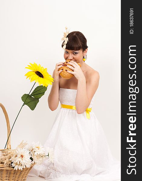 Beautiful brunette girl with ears of wheat in her hair is eating a bread isolated on the white background. Beautiful brunette girl with ears of wheat in her hair is eating a bread isolated on the white background