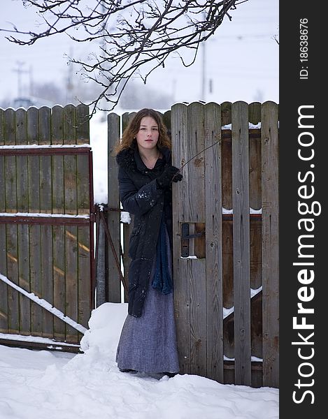 Beautiful young girl in long dress and coat near wooden fence in winter. Beautiful young girl in long dress and coat near wooden fence in winter