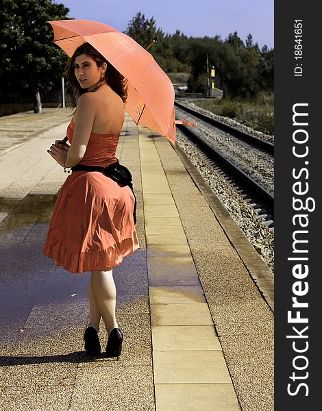 View of a beautiful woman with red dress and umbrella on a train station. View of a beautiful woman with red dress and umbrella on a train station.