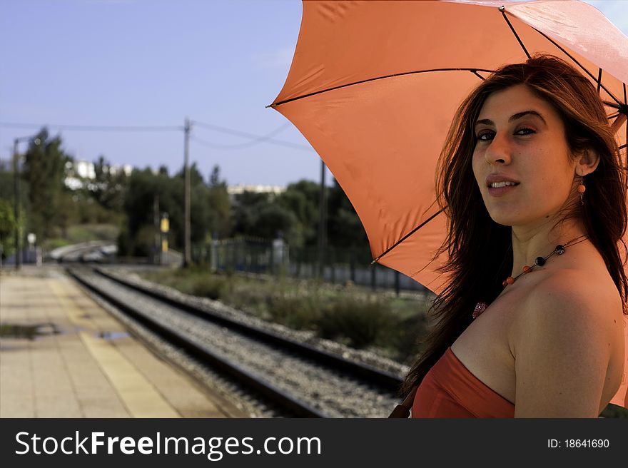 View of a beautiful woman with red dress and umbrella on a train station. View of a beautiful woman with red dress and umbrella on a train station.