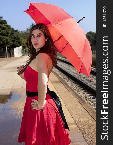 View of a beautiful woman with red dress and umbrella on a train station. View of a beautiful woman with red dress and umbrella on a train station.