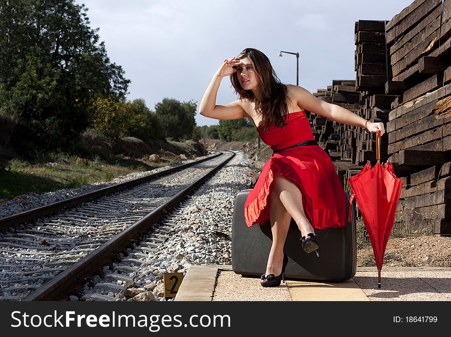 View of a beautiful woman with red dress and umbrella on a train station. View of a beautiful woman with red dress and umbrella on a train station.
