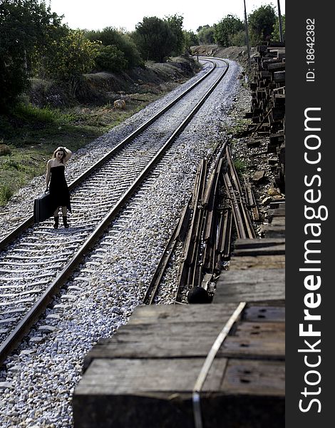 View of a beautiful woman with black dress with a travel case on a train track.