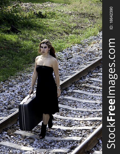 View of a beautiful woman with black dress with a travel case on a train track.