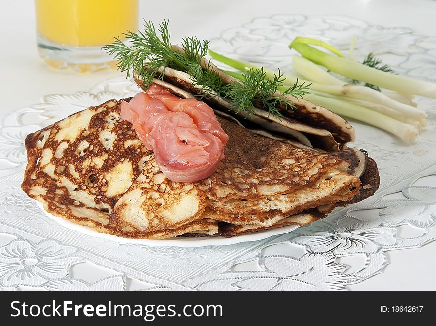 On a table there is a plate with pancakes and red fish. On a light background. On a table there is a plate with pancakes and red fish. On a light background