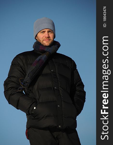 Attractive man with beard poses in warm jacket on cold winter's day, against bright blue sky. Attractive man with beard poses in warm jacket on cold winter's day, against bright blue sky