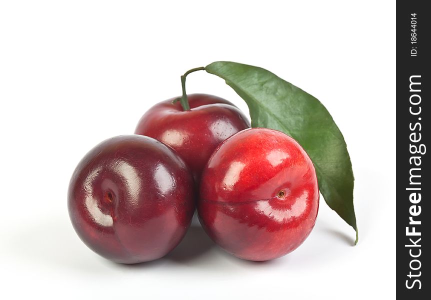 Three ripe plums with green leaf on white background