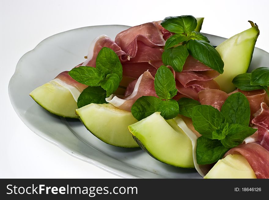 Melon with italian ham and basil leaves on porcelain dish. Melon with italian ham and basil leaves on porcelain dish