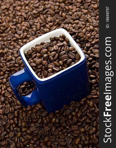 Dark blue cup with coffee grains on a small group of grains. Dark blue cup with coffee grains on a small group of grains