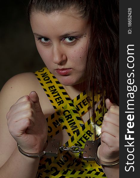 Portrait of young woman with police crime scene tape on body and handcuffs; black background. Portrait of young woman with police crime scene tape on body and handcuffs; black background.