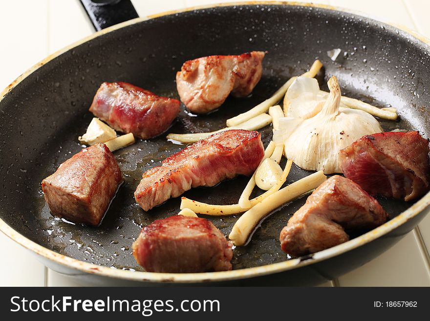 Chunks of pork and garlic on a frying pan. Chunks of pork and garlic on a frying pan