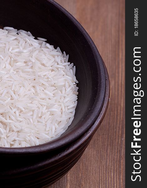 Uncooked rice in brown ceramic bowl on wooden background. Uncooked rice in brown ceramic bowl on wooden background