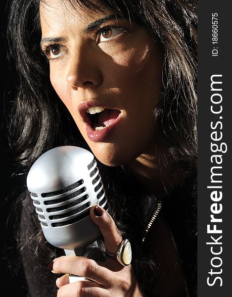 Portrait of young brunette beauty singing with retro microphone isolated on black