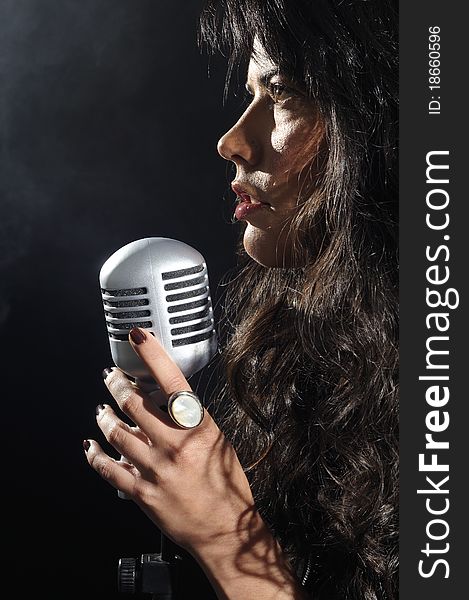 Portrait of young brunette beauty singing with retro microphone isolated on black