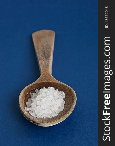Sea salt in wooden spoon on blue background