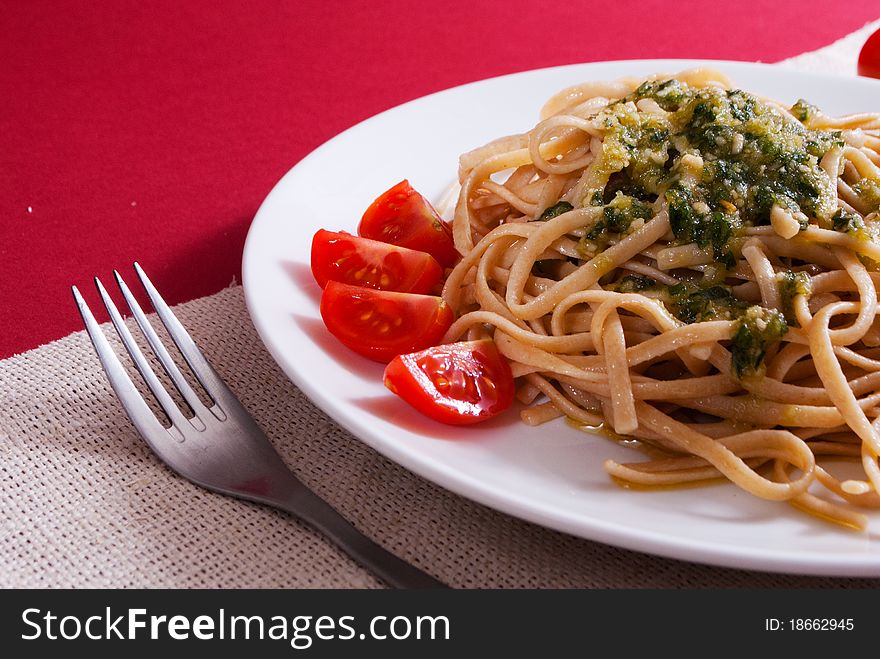 Pasta with pesto sause on a top with cherry tomatos decoration on red background. Pasta with pesto sause on a top with cherry tomatos decoration on red background