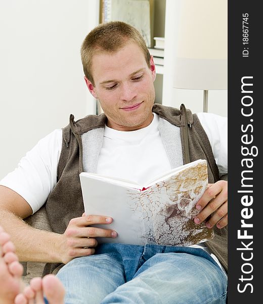 Young adult reading a book while he's lying on the couch. Young adult reading a book while he's lying on the couch